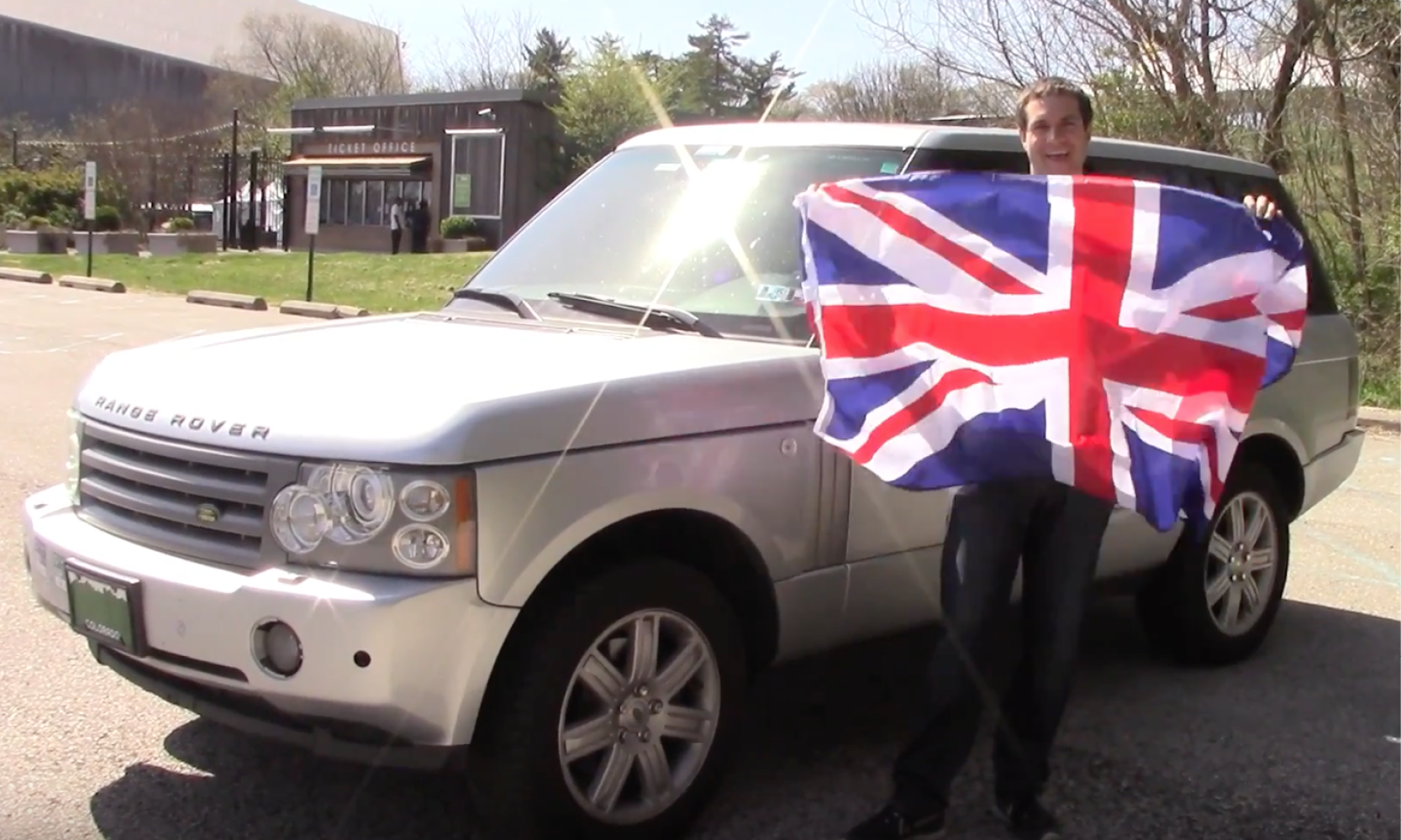 En man håller en brittisk flagga framför en Land Rover. (AI text)