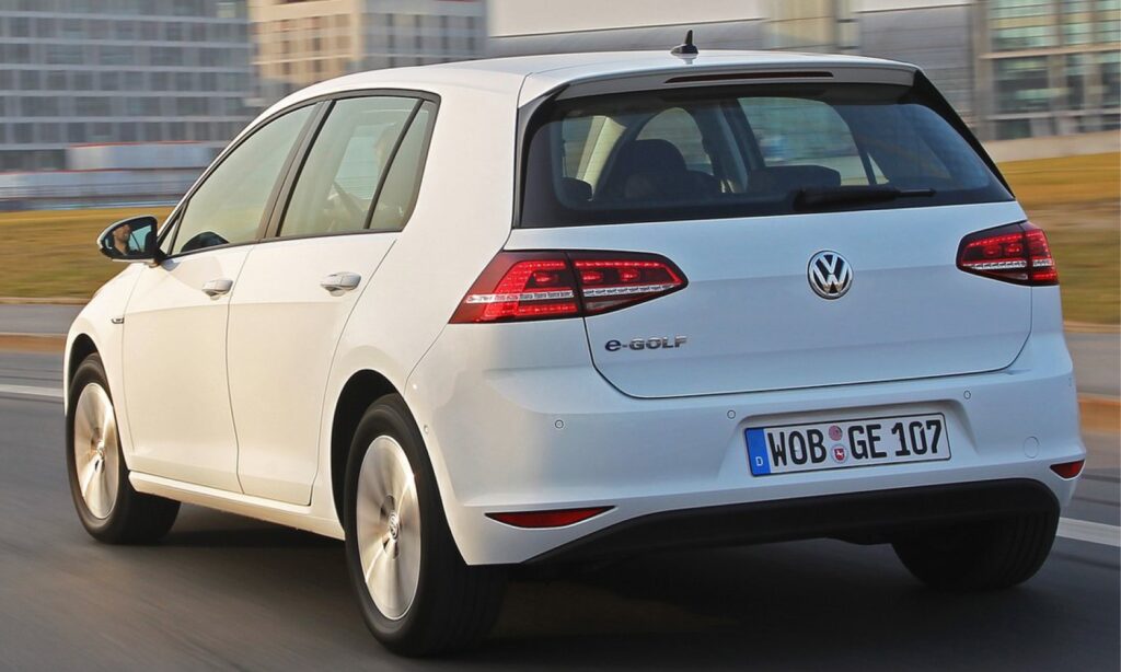 En vit Volkswagen Golf kör nedför en stadsgata. (AI text)