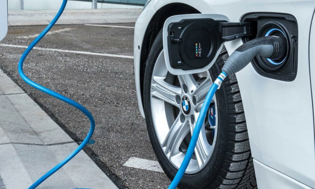 En vit BMW i3 elbil är uppkopplad till en elladdare. (AI text)
