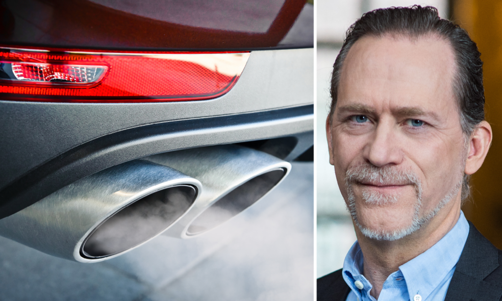 En man i kostym och slips står bredvid en bil med utluftningsrör. (AI text)