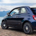 En Fiat 500 cabriolet parkerad på en gata mittemot en sjö. (AI text)