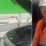 En man i orange säkerhetsväst och orange huvudsäkerhetsboll står bredvid en bil. (AI text)