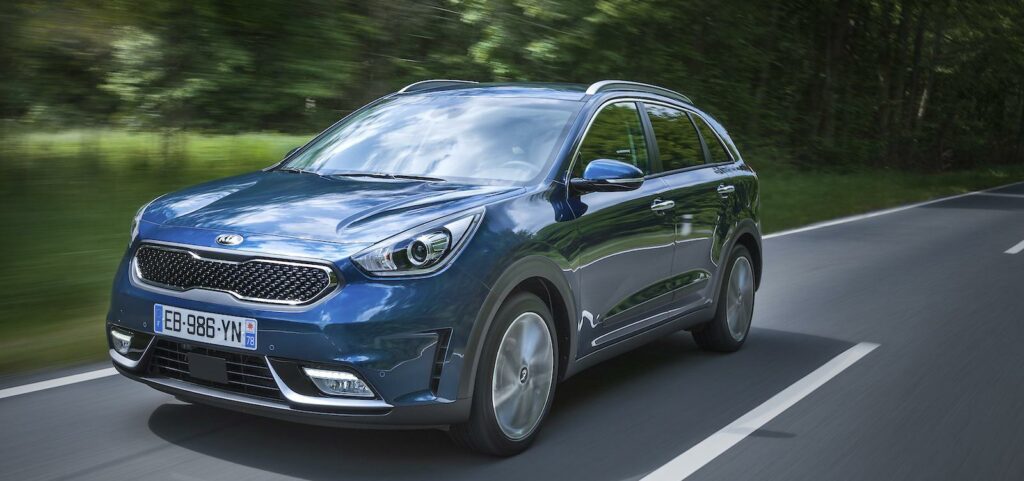 En blå Kia Niro kör nerför en landsväg. (AI text)