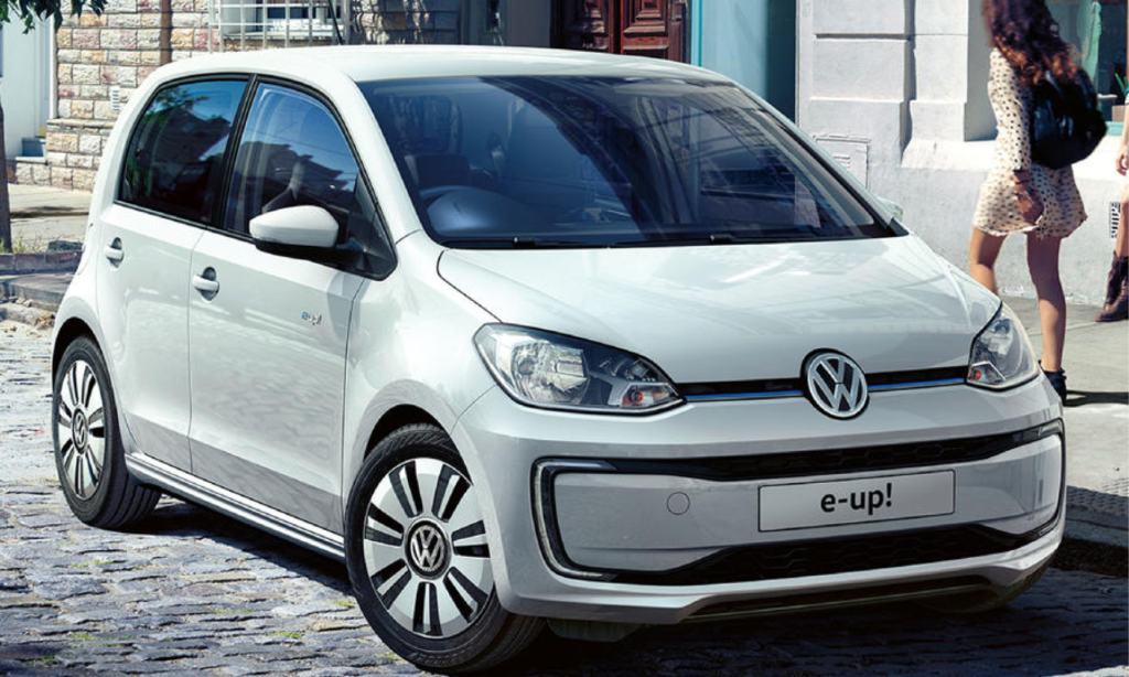 En vit Volkswagen up! parkerad på en ggråstensgata. (AI text)