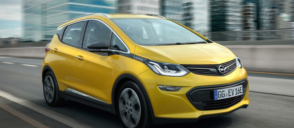 En gul Opel bil kör nerför en stadsgata. (AI text)