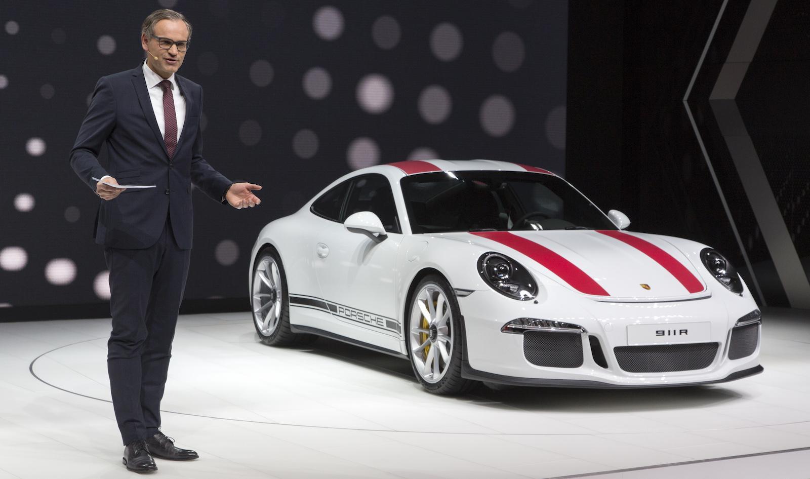 En man i kostym står bredvid en vit Porsche 911 GTS. (AI text)