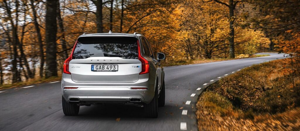 En Volvo XC90 SUV kör längs en landsväg på hösten. (AI text)