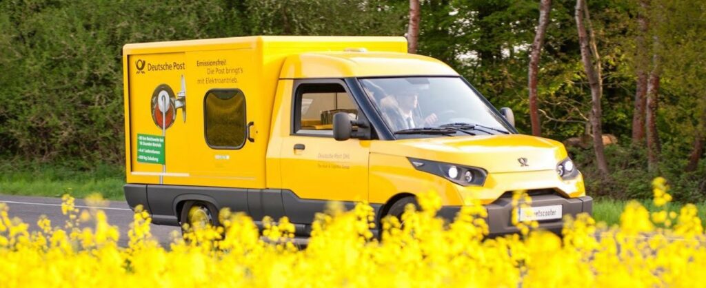 En gul lastbil kör ner en väg med gula blommor. (AI text)