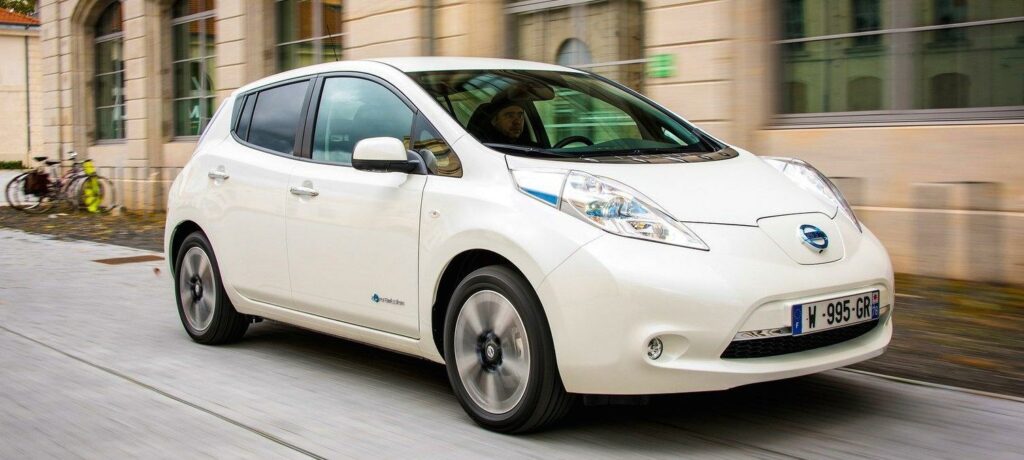 En vit Nissan Leaf kör nerför en stadsgata. (AI text)