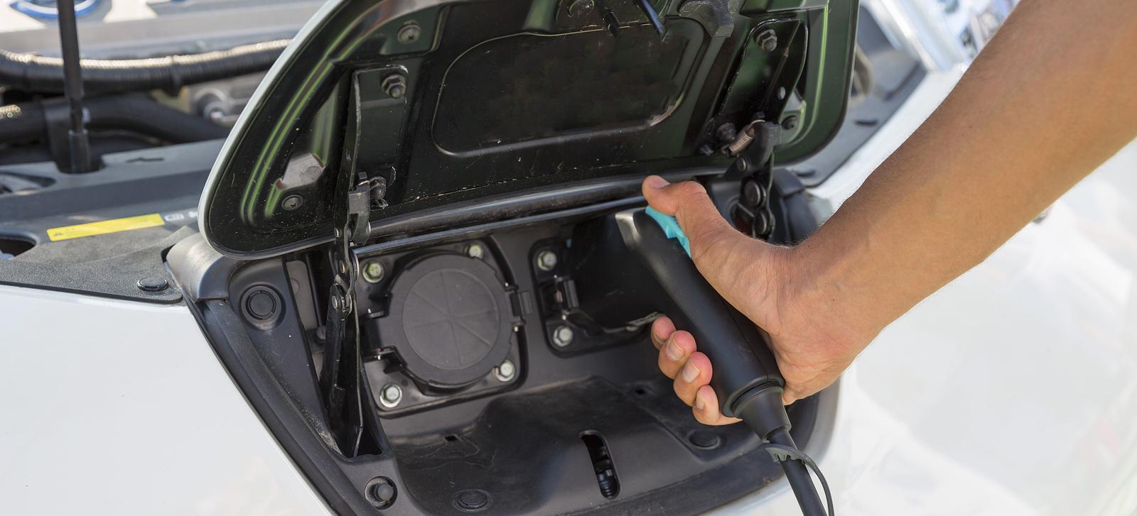 En man tar pluggen till en bil och stoppar den i en eluttag. (AI text)