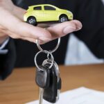 En man håller en gul bilnyckel och en papper med en bil tecknad på det. (AI text)