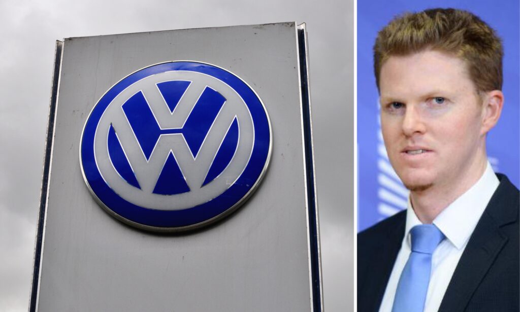 En man i kostym och slips står bredvid en Volkswagen-logotyp. (AI text)