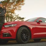 En man står bredvid en röd Ford Mustang. (AI text)