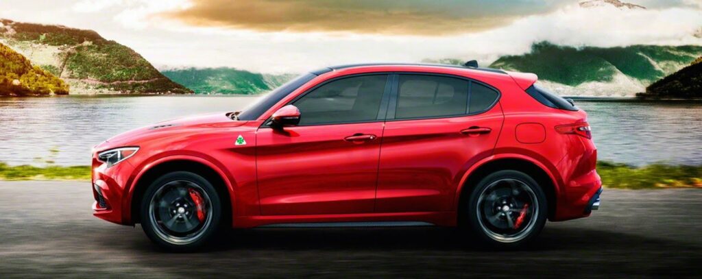 En röd Alfa Romeo SUV kör nerför en väg med berg i bakgrunden. (AI text)