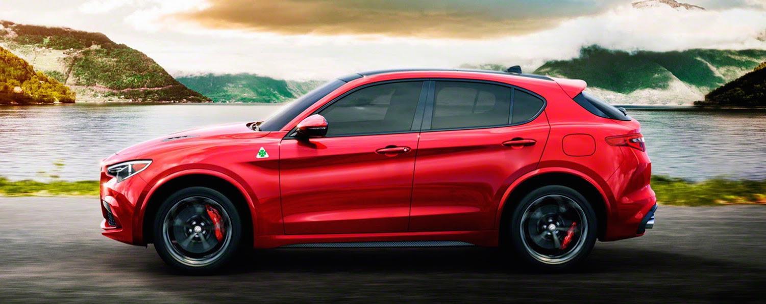 En röd Alfa Romeo SUV kör nerför en väg med berg i bakgrunden. (AI text)