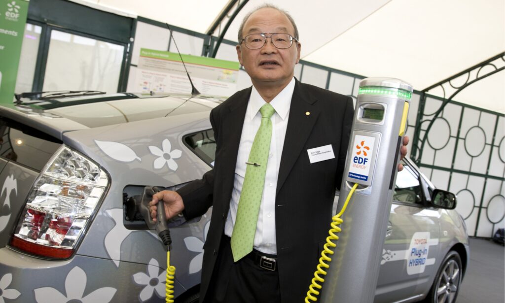 En man i kostym och slips laddar sin elbil. (AI text)