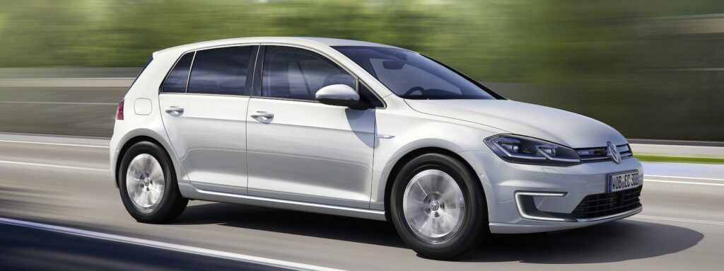 En vit Volkswagen Golf E - EV kör nedför en väg. (AI text)