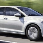 En vit Volkswagen Golf E - EV kör nedför en väg. (AI text)