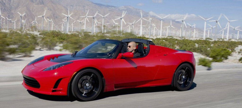 En röd Tesla sportbil kör nerför en krökig väg. (AI text)