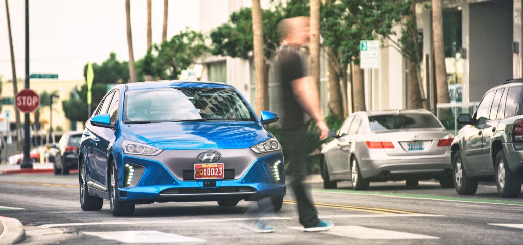 En man kryssar gatan framför en blå bil. (AI text)