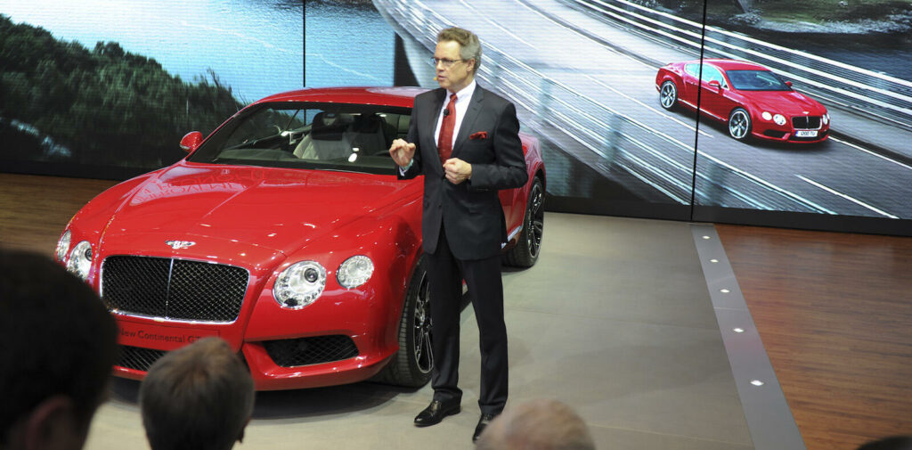 En man står framför en röd Bentley Continental GT. (AI text)