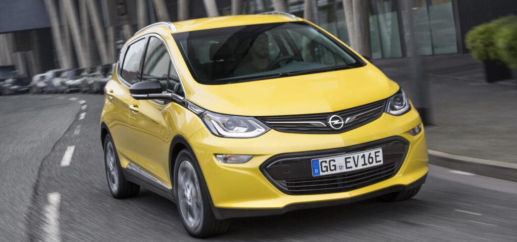 En gul Opel Astra kör nedför en stadsgata. (AI text)