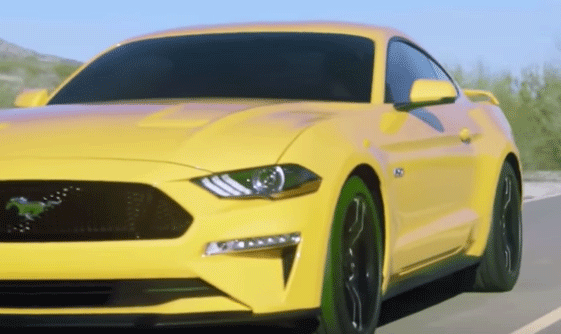 En gul Ford Mustang GT kör längs en väg. (AI text)