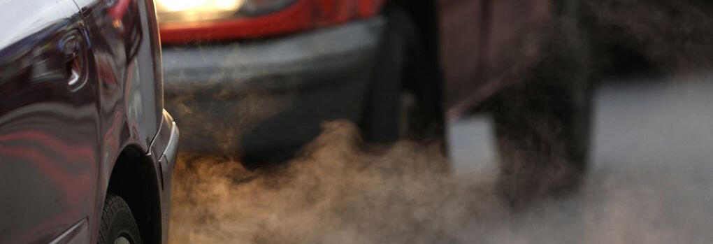 En bil kör nedför en gata med rök som kommer ut ifrån den. (AI text)