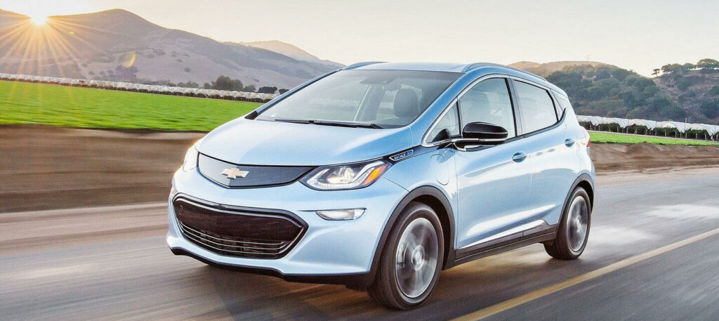 En blå Chevrolet Bolt EV kör längs en landsväg. (AI text)