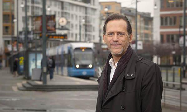 En man i en rock står framför en stadsgata. (AI text)