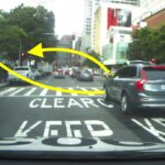 En bil körs nedför en stadsgata med en stoppskylt i sikte. (AI text)