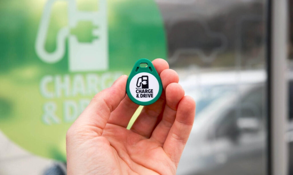 En person håller en grönt laddningsenheter framför en grönt skylt. (AI text)