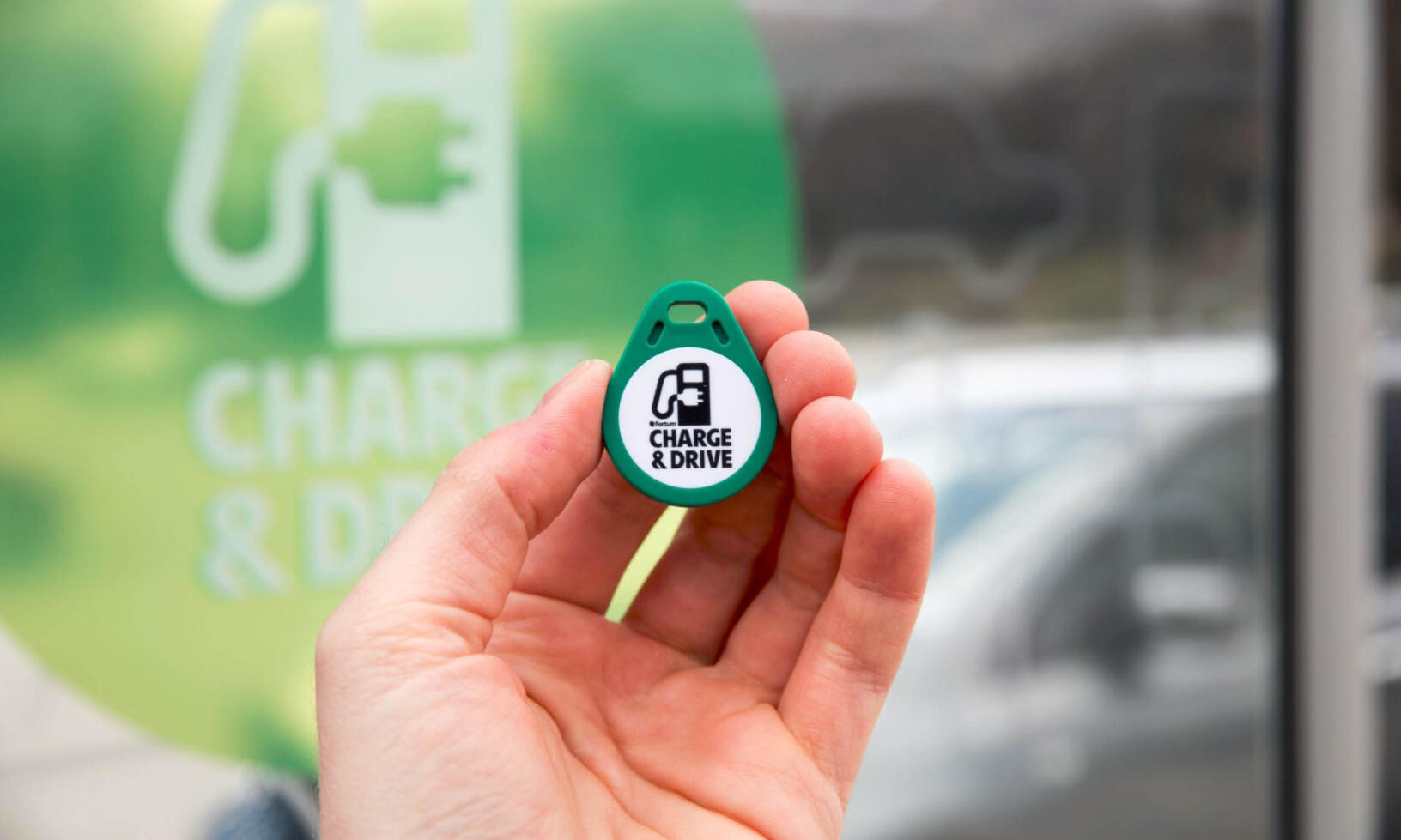 En person håller en grönt laddningsenheter framför en grönt skylt. (AI text)