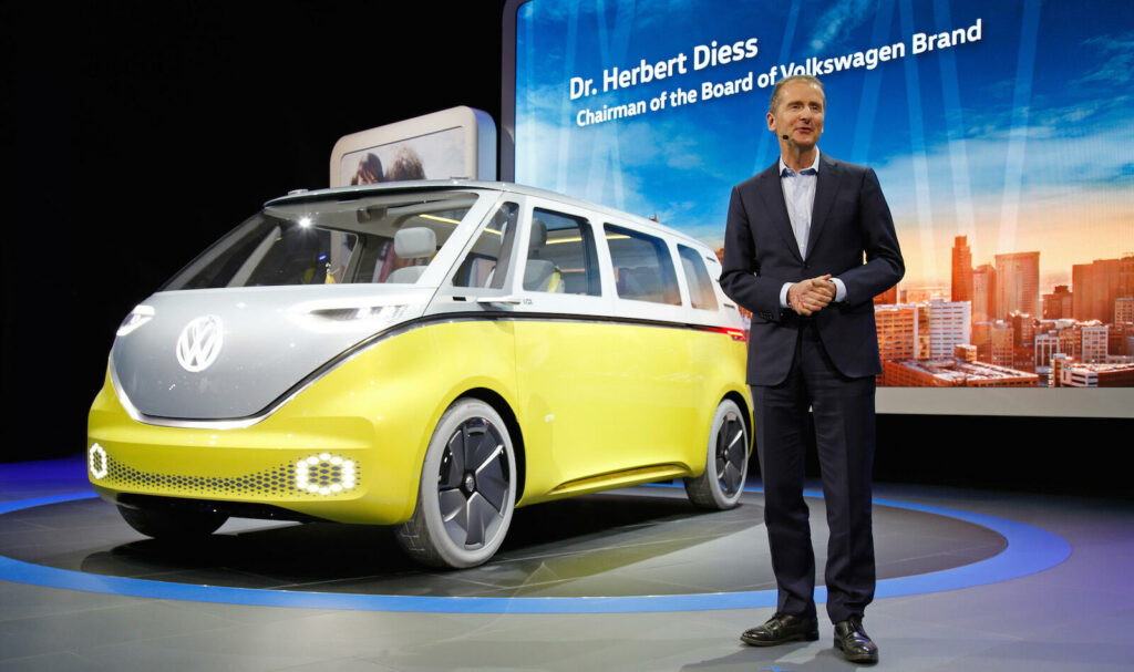 En man i kostym står bredvid en Volkswagen-van. (AI text)