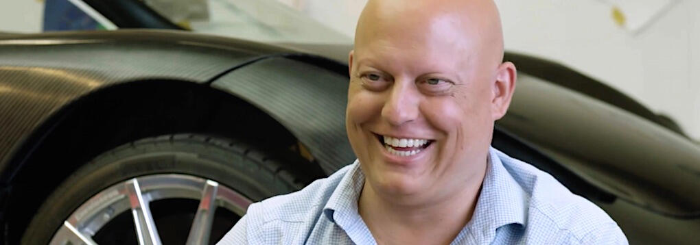 En man leker ett leende framför en bil. (AI text)