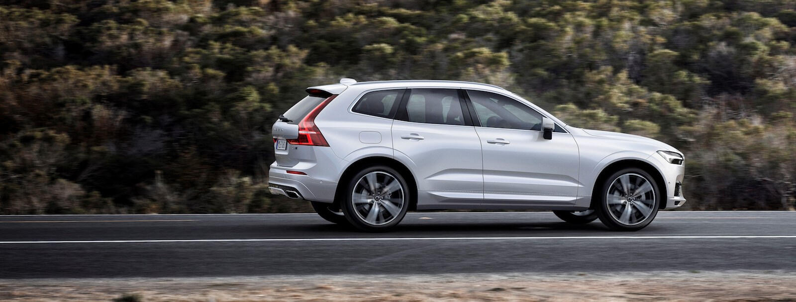 En vit Volvo XC90 SUV kör nerför en bergsväg. (AI text)