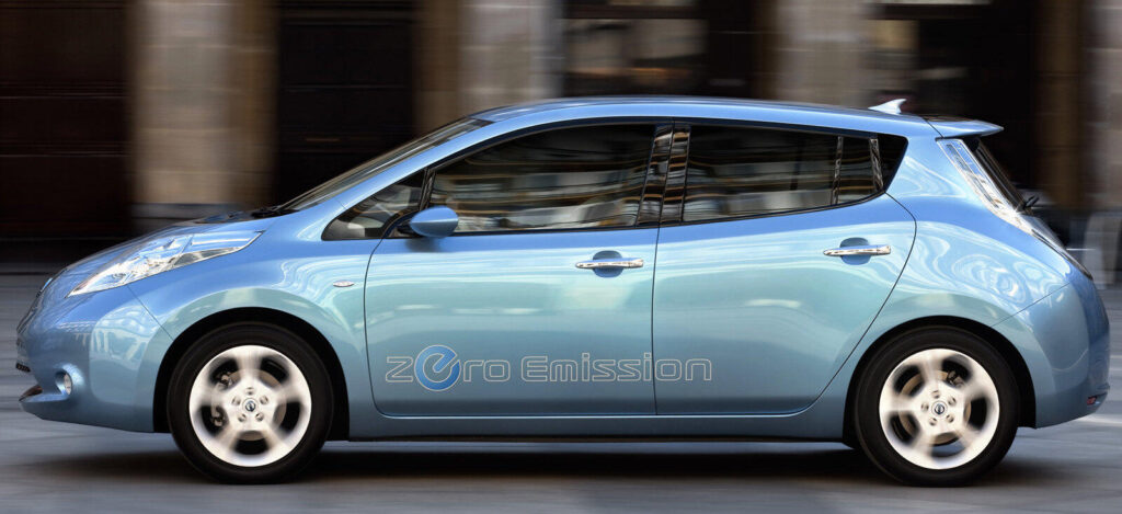 En blå Nissan Leaf elbil kör nerför en stadsgata. (AI text)