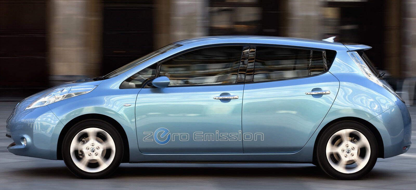 En blå Nissan Leaf elbil kör nerför en stadsgata. (AI text)