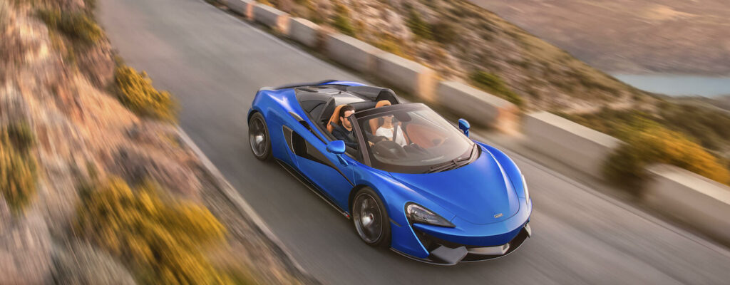 En blå McLaren-sportsbil kör nedför en bergväg. (AI text)