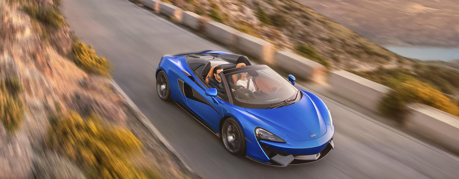 En blå McLaren-sportsbil kör nedför en bergväg. (AI text)