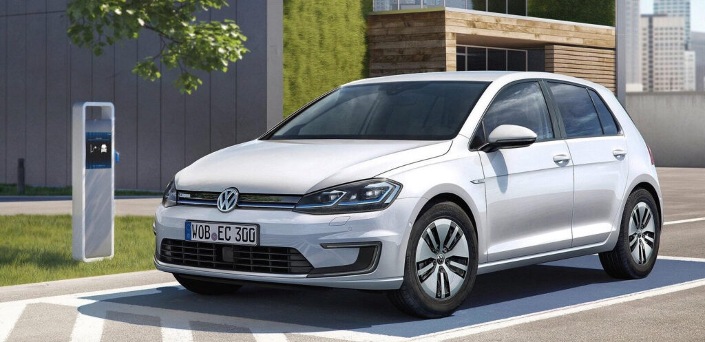 En vit Volkswagen Golf parkerad vid en elbilsladdstation. (AI text)