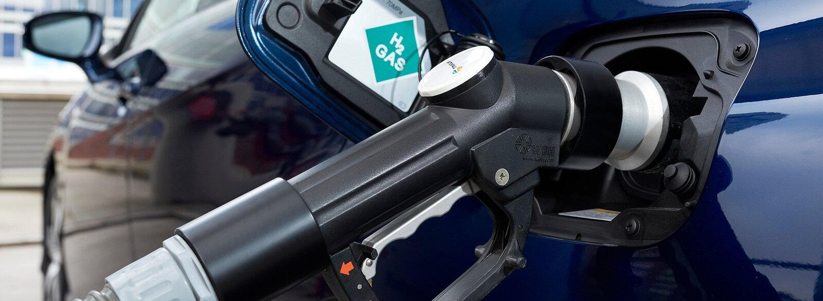 En blå bil står parkerad vid en bensinstation. (AI text)