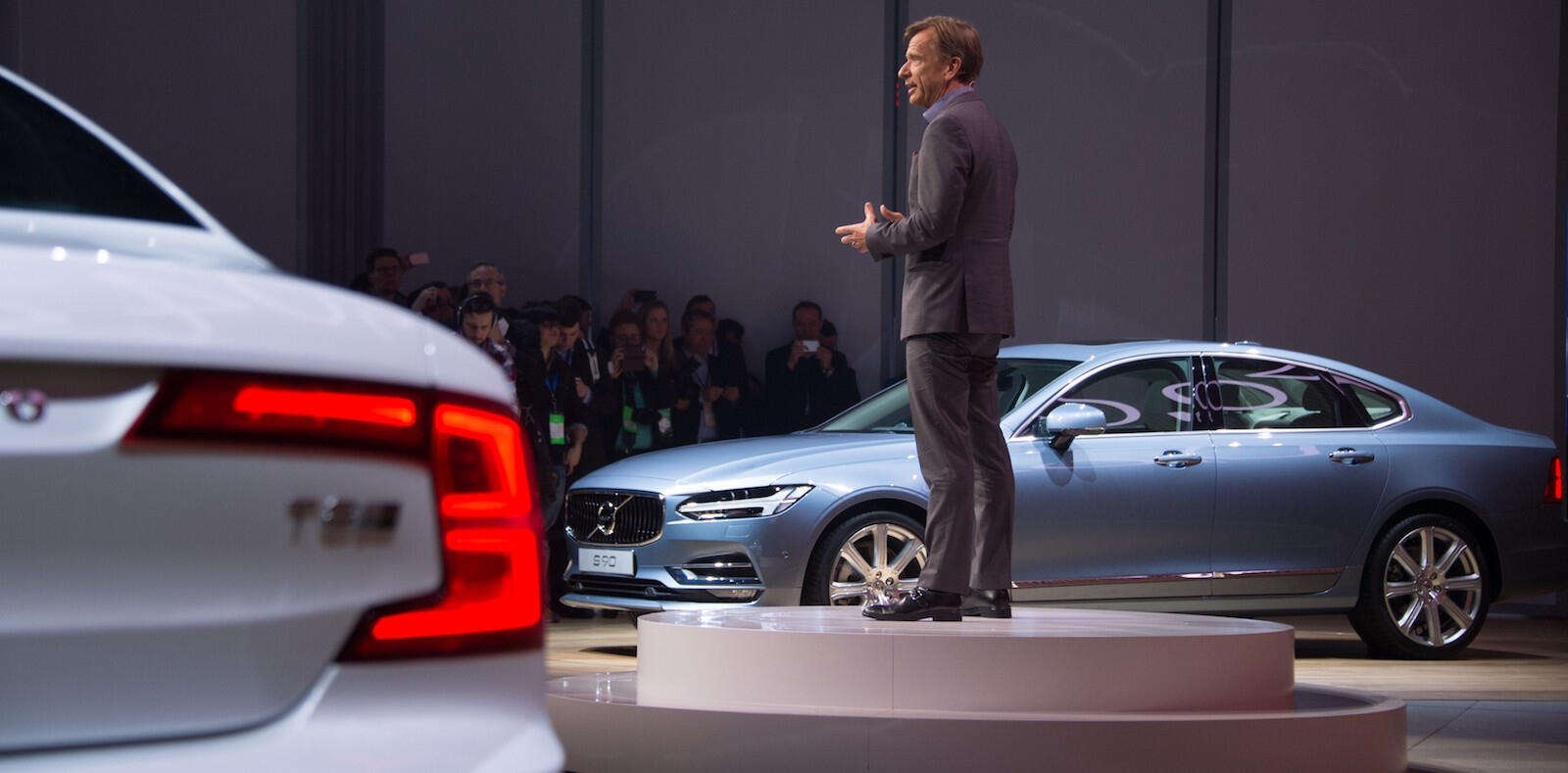 En man står på scenen framför en bil. (AI text)