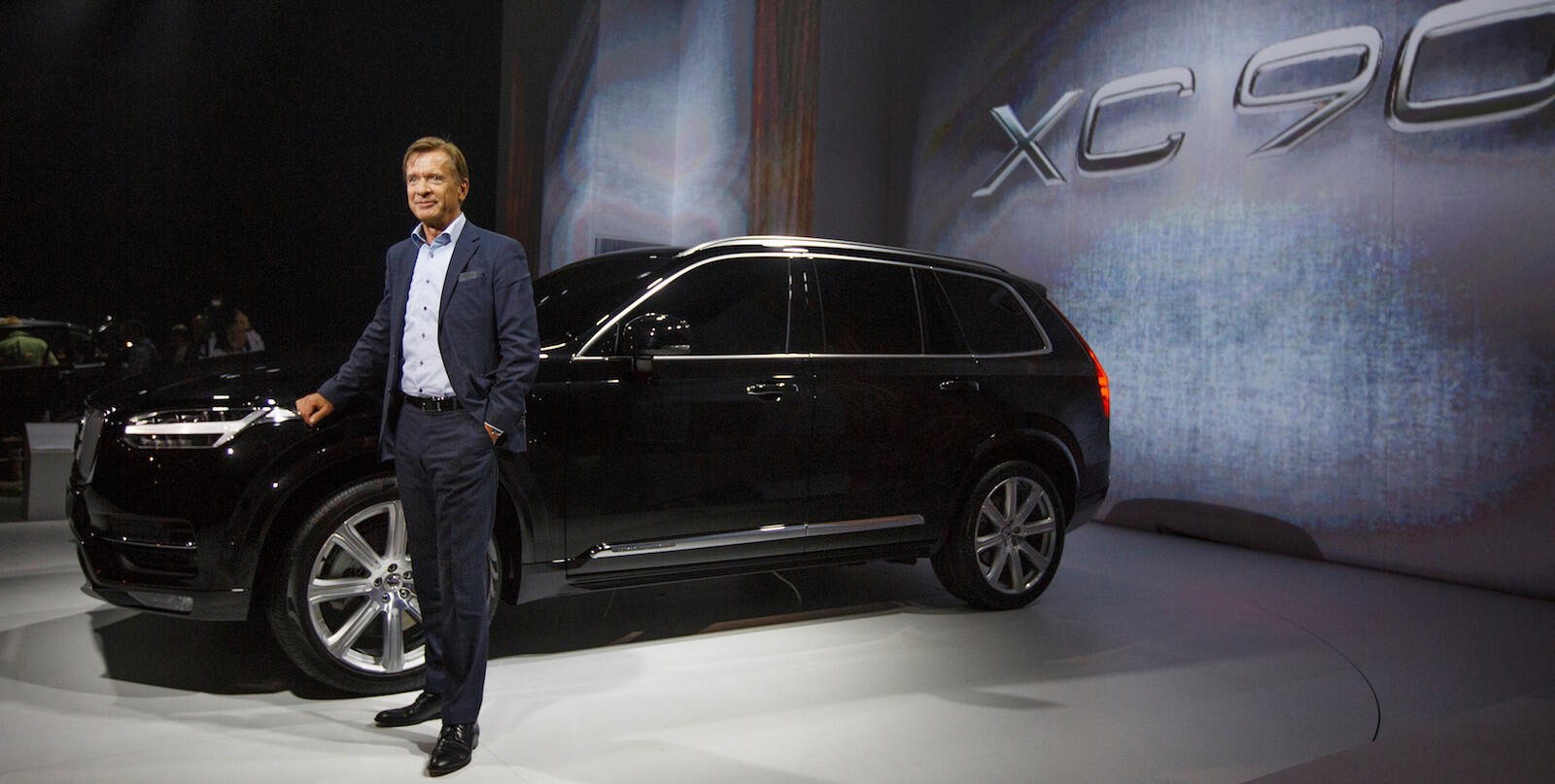 En man står bredvid en Volvo XC90 SUV på Shanghais bilsalong. (AI text)