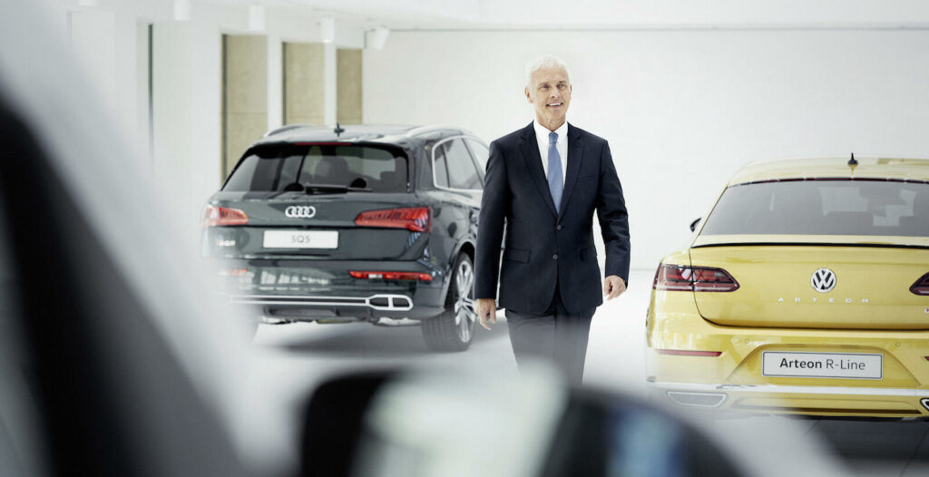 En man i kostym går förbi en rad bilar. (AI text)