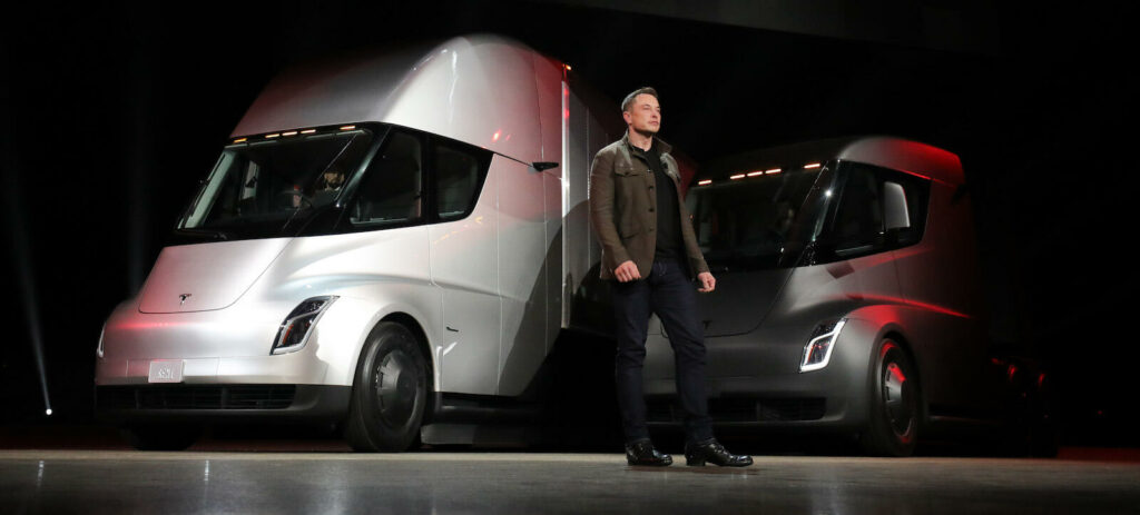 En Tesla-ansikte står bredvid två Tesla-lastbilar. (AI text)