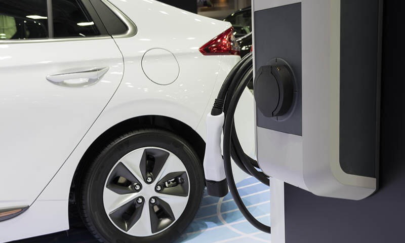 En vit bil är uppladdad i en elbilsladdare på en bilsalong. (AI text)