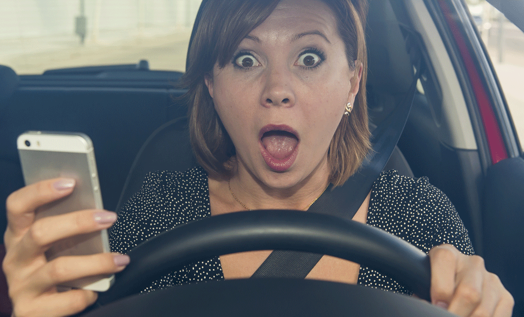 En kvinna kör bil och tittar på sin telefon. (AI text)