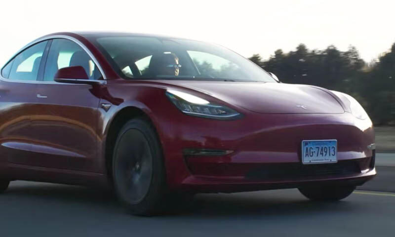 En Tesla Model 3 kör längs vägen. (AI text)