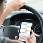 En kvinna kör en bil med en mobiltelefon i handen. (AI text)